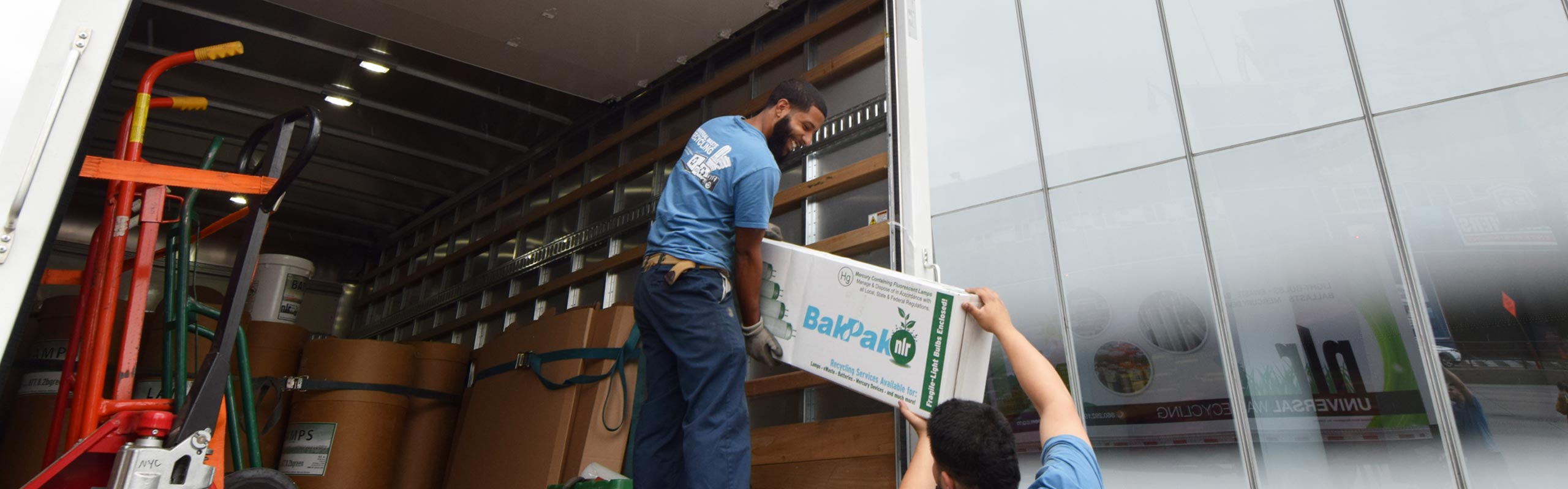 A picture of two of NLR's drivers moving a mailback box in New York City. NLR offers pick up and mailback programs for recycling lamps, batteries, electronic waste, and other universal waste.